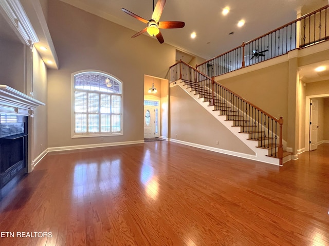 unfurnished living room with hardwood / wood-style floors, ceiling fan, and a high ceiling