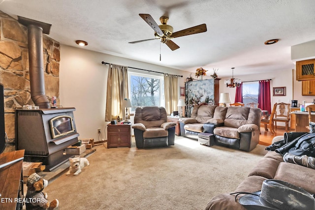 living room featuring ceiling fan, a wood stove, a textured ceiling, and carpet flooring