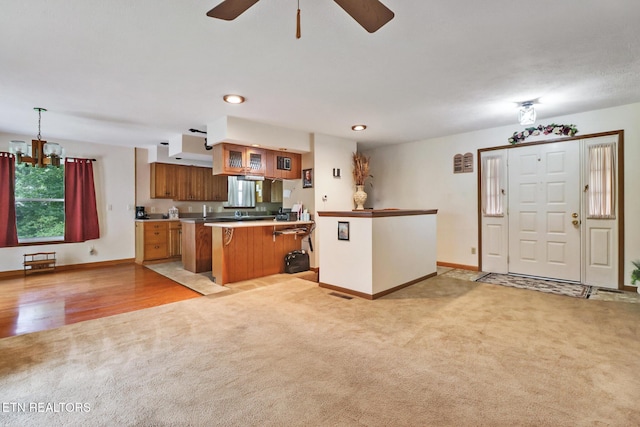 27 Brambleton Ct, Crossville, TN 38558 - kitchen with light carpet, a peninsula, brown cabinetry, a chandelier, and ceiling fan