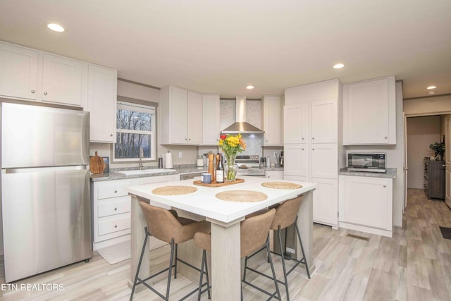 kitchen with a sink, white cabinetry, appliances with stainless steel finishes, wall chimney exhaust hood, and light countertops