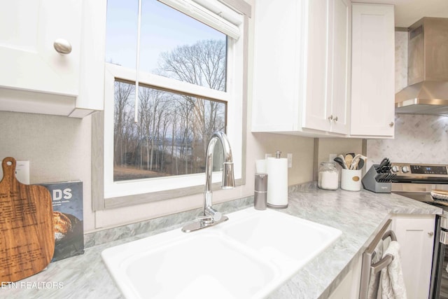 kitchen featuring a sink, stainless steel range with electric cooktop, wall chimney exhaust hood, white cabinets, and decorative backsplash