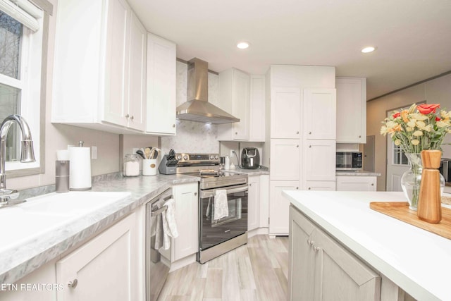 kitchen with light countertops, wall chimney range hood, white cabinets, and stainless steel appliances