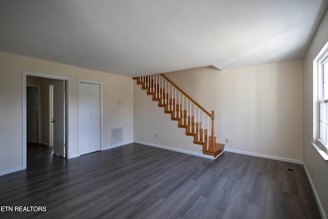 empty room with dark wood-style floors, a wealth of natural light, visible vents, and stairway