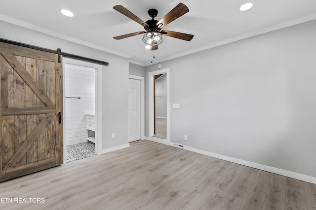 unfurnished bedroom with ensuite bath, ornamental molding, light hardwood / wood-style floors, and a barn door