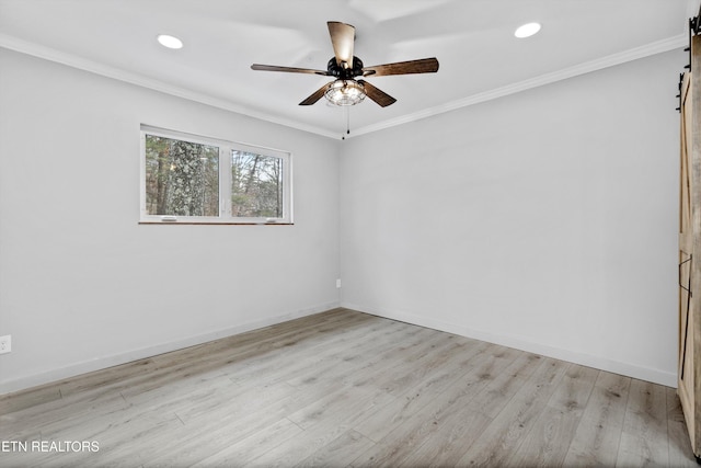 spare room featuring crown molding, light hardwood / wood-style floors, a barn door, and ceiling fan