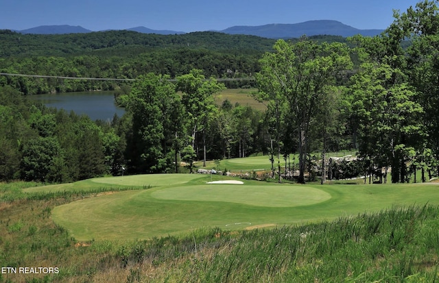 view of property's community featuring a water and mountain view, a wooded view, a lawn, and view of golf course