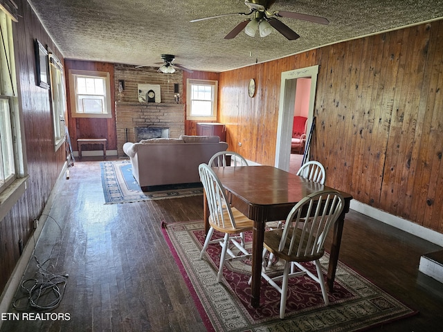 dining space featuring a fireplace, dark hardwood / wood-style floors, a textured ceiling, and wood walls