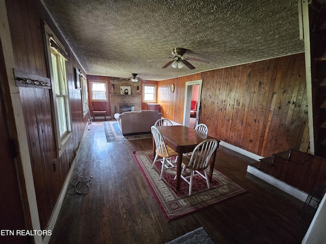 dining space with wood walls, hardwood / wood-style flooring, ceiling fan, a brick fireplace, and a textured ceiling