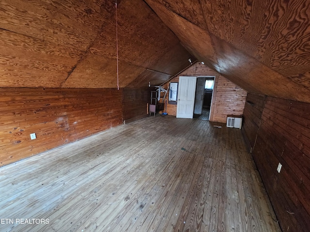 additional living space with lofted ceiling, wood-type flooring, and wooden walls