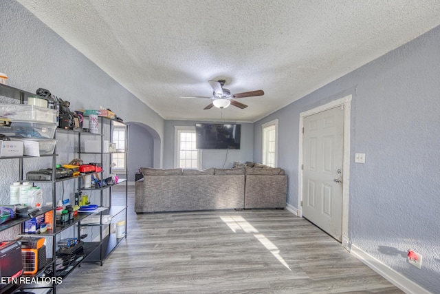 living room with ceiling fan, a textured ceiling, and light wood-type flooring