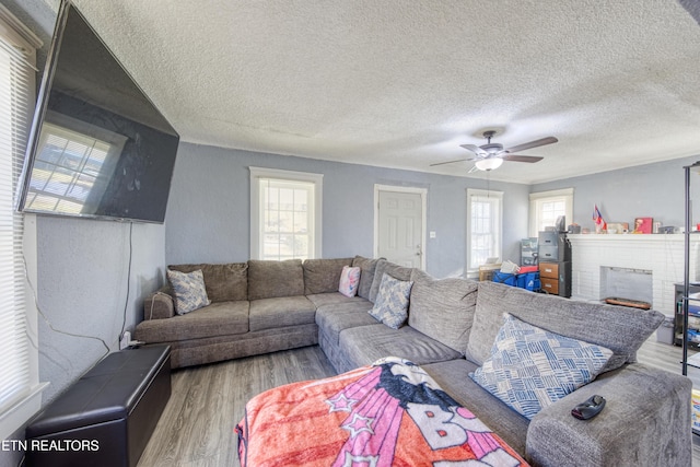 living room with a brick fireplace, a textured ceiling, wood-type flooring, and ceiling fan