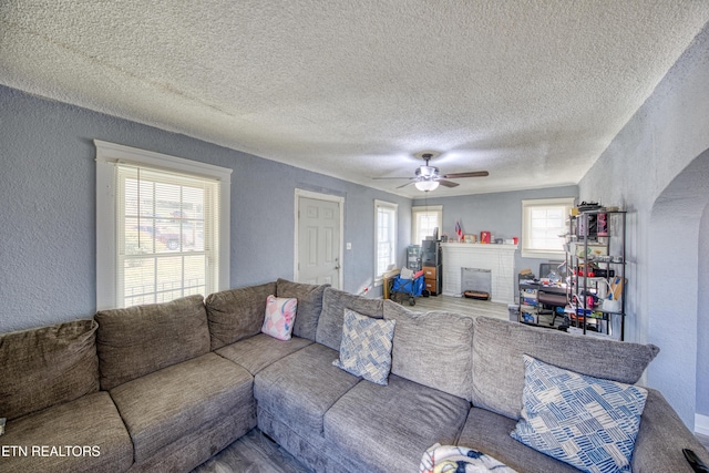 living room featuring ceiling fan, a textured ceiling, and a fireplace