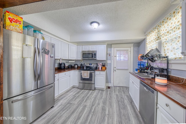 kitchen featuring sink, wooden counters, appliances with stainless steel finishes, light hardwood / wood-style floors, and white cabinets