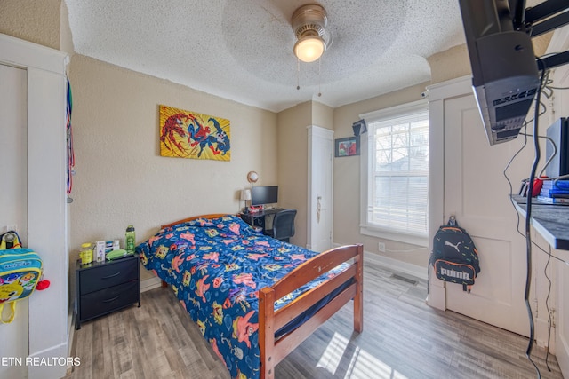 bedroom featuring ceiling fan, light hardwood / wood-style floors, and a textured ceiling