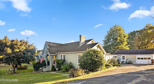 view of front of property featuring a garage, driveway, a chimney, and a front yard