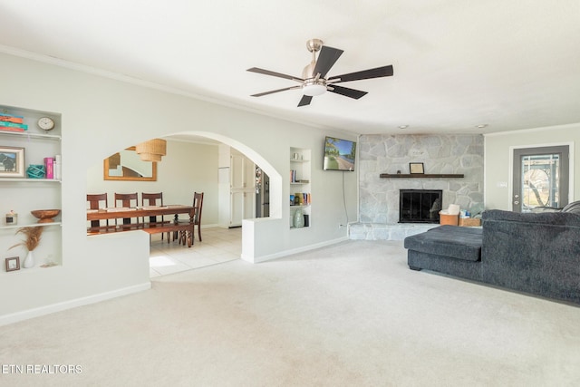 living room featuring built in features, ceiling fan, a fireplace, ornamental molding, and light colored carpet