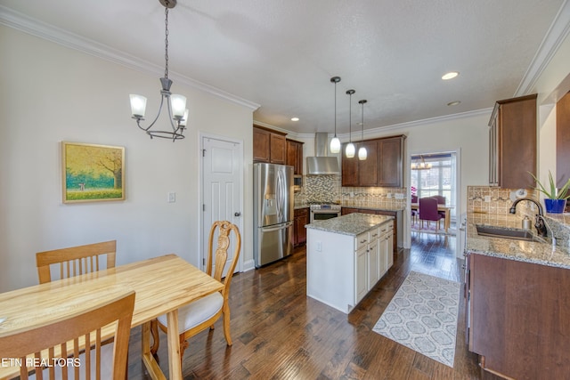 kitchen with decorative light fixtures, sink, stainless steel appliances, light stone countertops, and wall chimney range hood