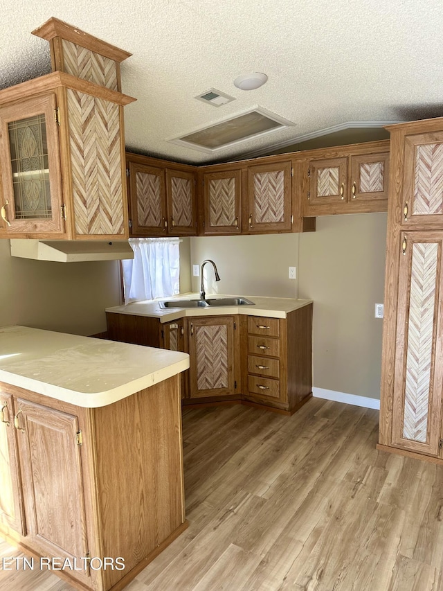 kitchen with sink, a textured ceiling, light hardwood / wood-style floors, and kitchen peninsula