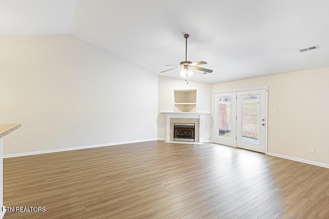 unfurnished living room featuring light hardwood / wood-style flooring, vaulted ceiling, a tile fireplace, and ceiling fan