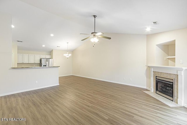 unfurnished living room with a tiled fireplace, ceiling fan with notable chandelier, light hardwood / wood-style flooring, and vaulted ceiling