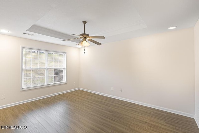 unfurnished room featuring dark hardwood / wood-style floors, ceiling fan, and a tray ceiling