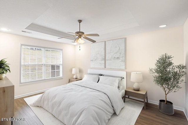 bedroom with ceiling fan, dark hardwood / wood-style floors, and a raised ceiling