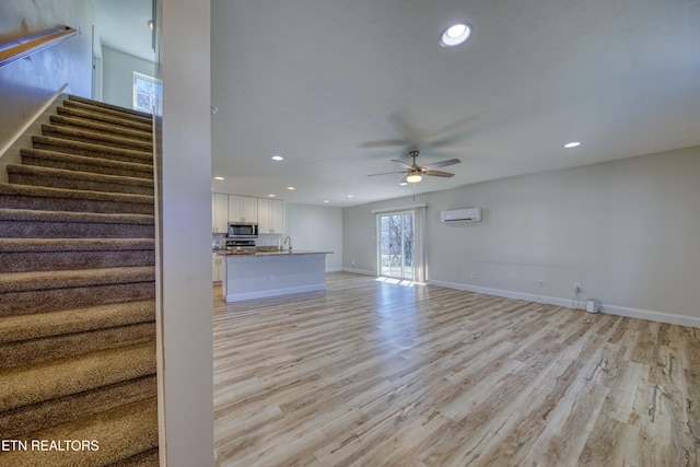 unfurnished living room with light wood finished floors, baseboards, stairway, a wall mounted air conditioner, and recessed lighting