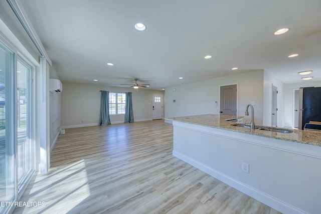 kitchen featuring light stone counters, recessed lighting, open floor plan, a sink, and a wall mounted air conditioner