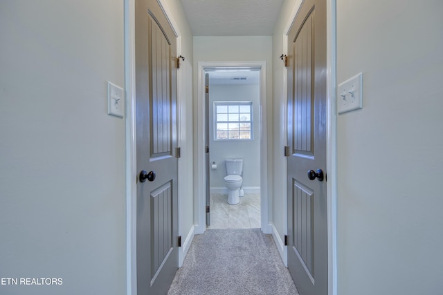 hallway with light carpet, baseboards, and a textured ceiling