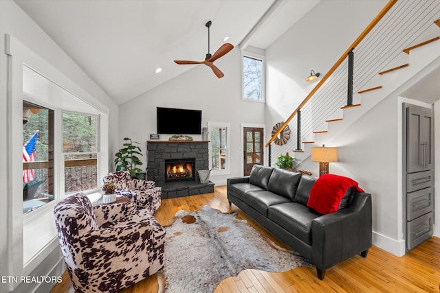 living room featuring high vaulted ceiling, a stone fireplace, hardwood / wood-style floors, and ceiling fan