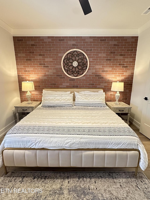 bedroom with ceiling fan, brick wall, hardwood / wood-style floors, and ornamental molding