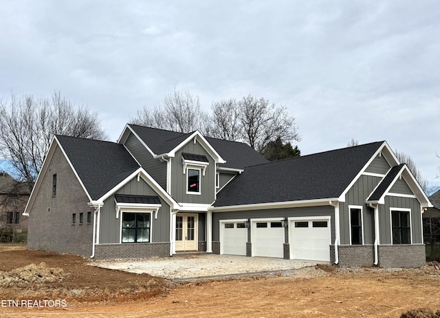 craftsman inspired home featuring brick siding, board and batten siding, roof with shingles, a garage, and driveway