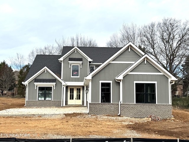 view of front facade with brick siding, french doors, a shingled roof, and board and batten siding