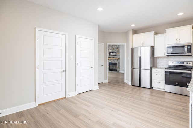 kitchen featuring appliances with stainless steel finishes, a stone fireplace, white cabinetry, decorative backsplash, and light hardwood / wood-style floors