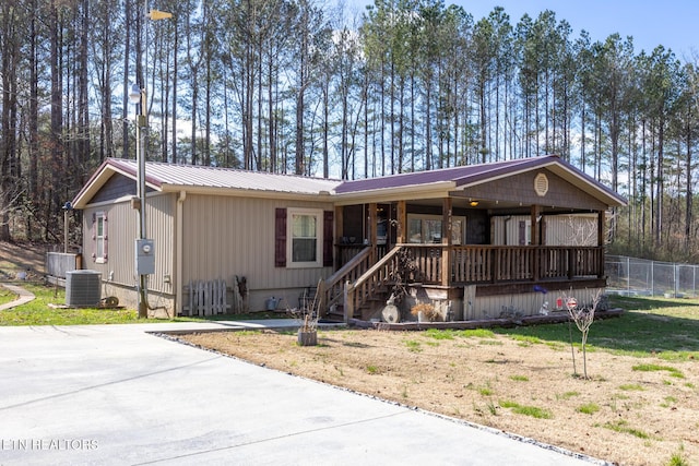 view of front facade featuring covered porch, metal roof, fence, cooling unit, and a front lawn