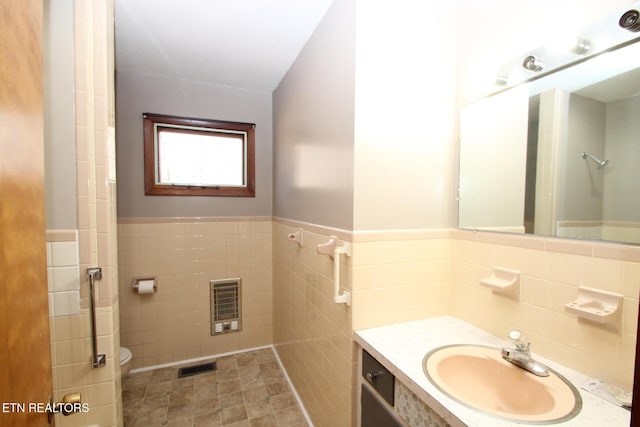 bathroom featuring toilet, heating unit, tile walls, vanity, and tile patterned flooring