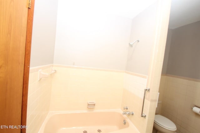 bathroom featuring tile walls, a tub to relax in, and toilet