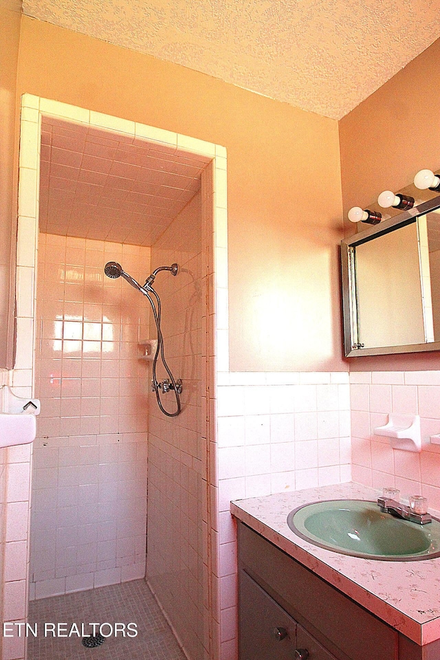 bathroom featuring a tile shower, vanity, tile walls, and a textured ceiling