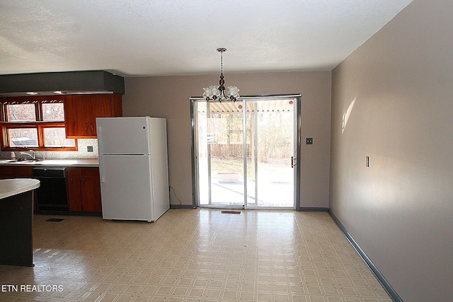 kitchen with sink, white refrigerator, black dishwasher, a notable chandelier, and pendant lighting