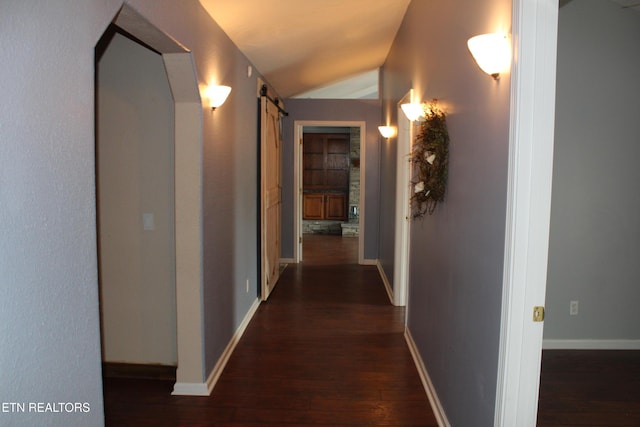 corridor with vaulted ceiling, a barn door, and dark hardwood / wood-style flooring