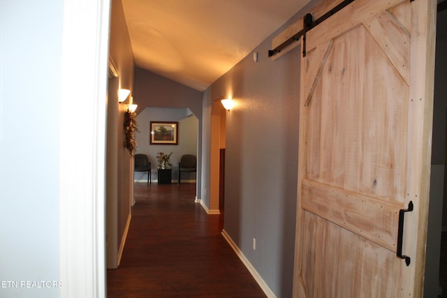 hall with a barn door, dark hardwood / wood-style floors, and vaulted ceiling