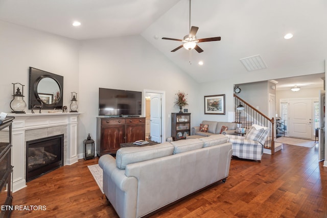 living room featuring ceiling fan, high vaulted ceiling, a tile fireplace, stairs, and dark wood finished floors