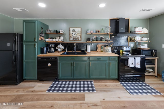 kitchen featuring sink, wall chimney range hood, light hardwood / wood-style floors, black appliances, and green cabinetry