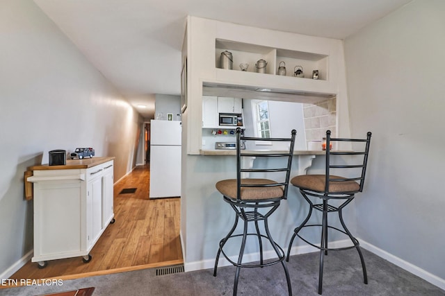 kitchen with white refrigerator, a kitchen breakfast bar, light hardwood / wood-style floors, and white cabinets