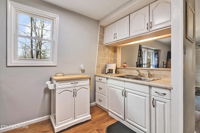 kitchen with tasteful backsplash, sink, white cabinets, and light hardwood / wood-style floors