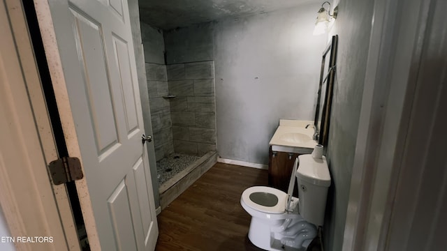 bathroom with wood-type flooring, a tile shower, vanity, and toilet