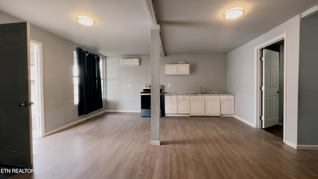 kitchen featuring dark wood-type flooring, sink, a wall unit AC, electric stove, and white cabinets