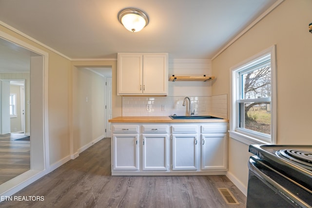 kitchen with butcher block countertops, sink, white cabinetry, hardwood / wood-style flooring, and backsplash