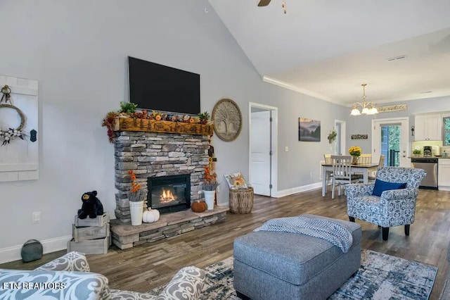 living room featuring hardwood / wood-style flooring, a stone fireplace, ceiling fan with notable chandelier, and high vaulted ceiling