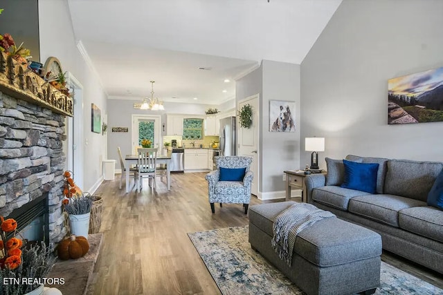 living room with crown molding, vaulted ceiling, a notable chandelier, a fireplace, and light hardwood / wood-style floors